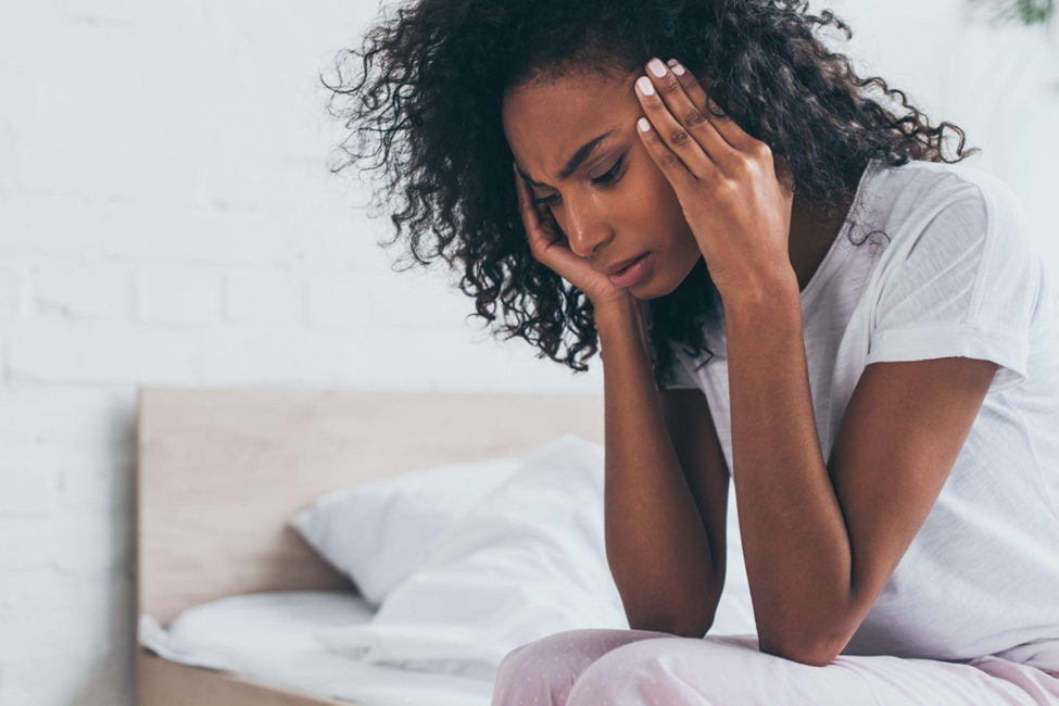 african american woman holding hands near head while suffering from headache in bedroom