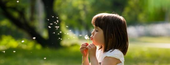 Girl blowing dandelion seeds outdoors on a sunny day