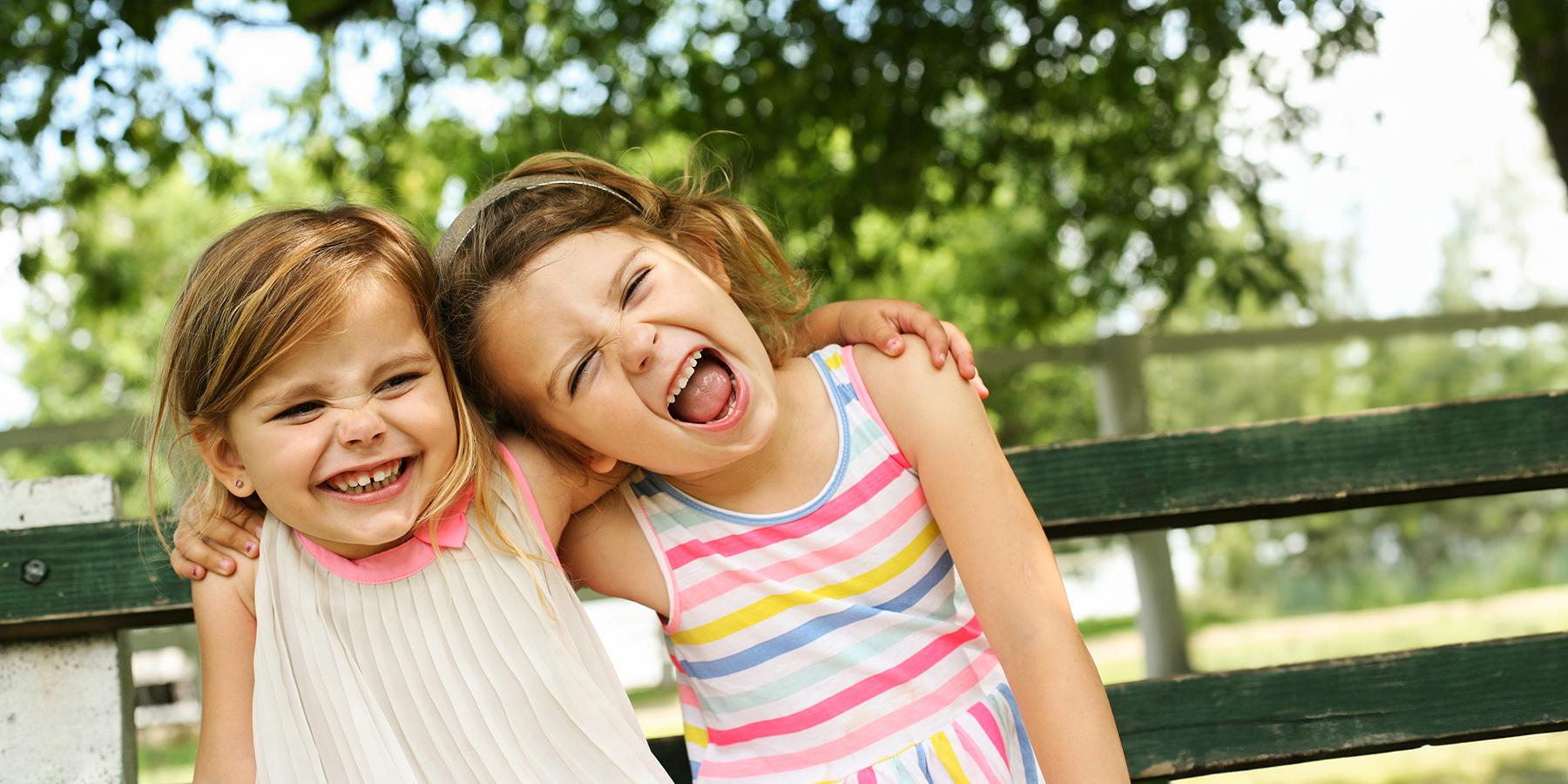 Two laughing children on a park bench with arms around each other