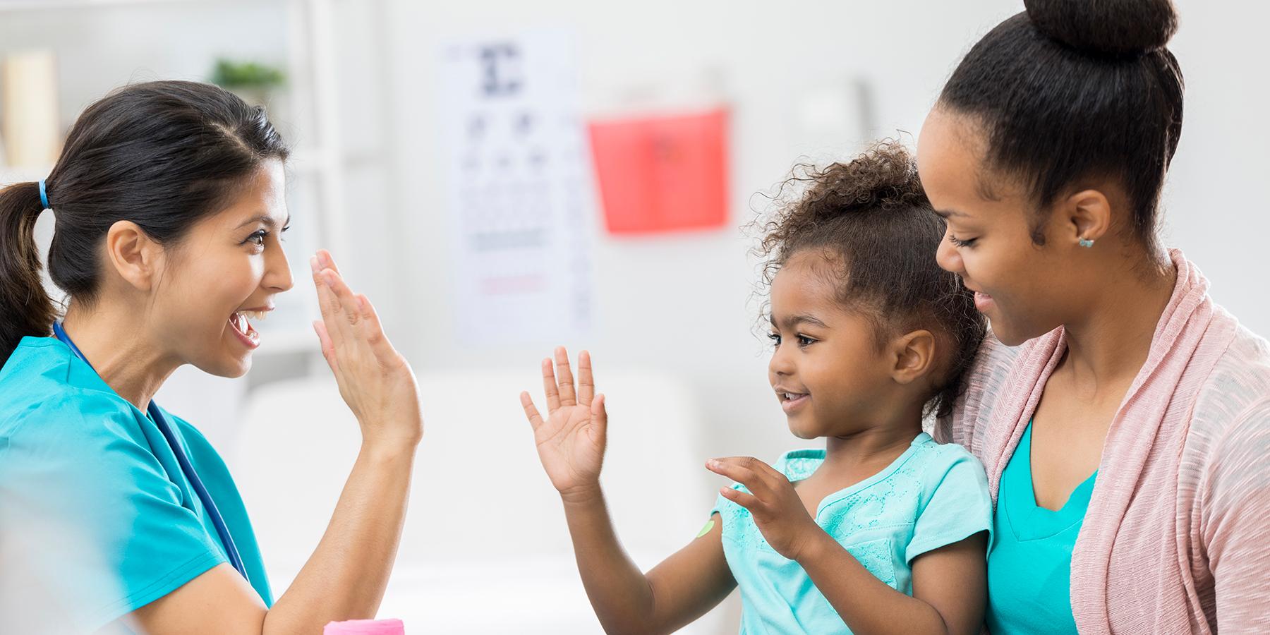 Caregiver holding smiling child who is giving a healthcare provider a high-five
