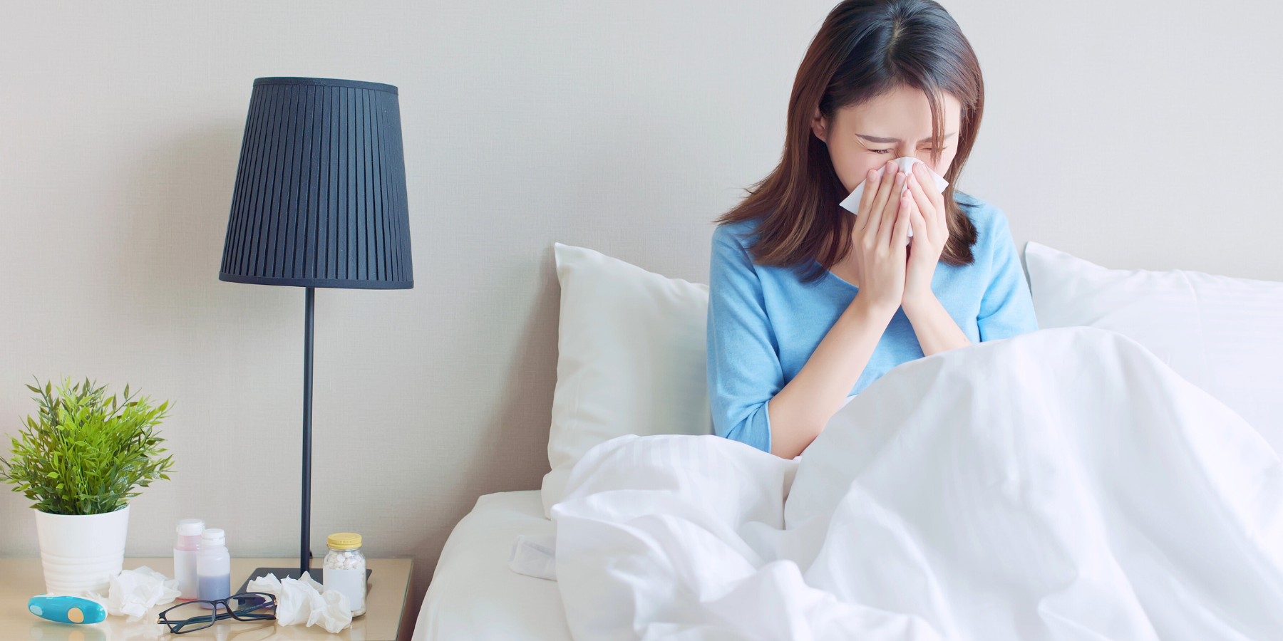 Woman sick in bed blowing her nose in a tissue