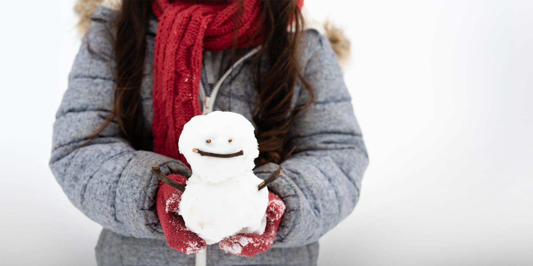 Girl holding tiny smiling snowman in her red mittens